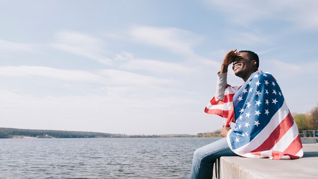 Man wrapped in American flag sitting dangling feet and closing eyes from sun 