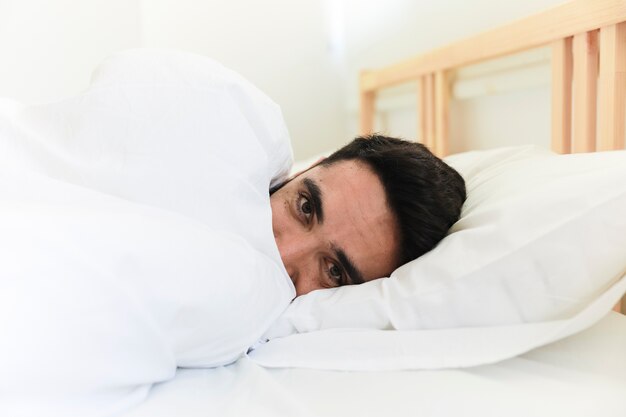 Man wrapped in blanket lying on bed