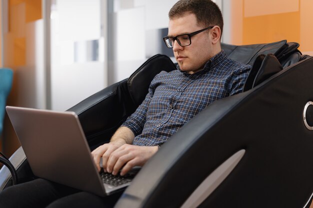 Man writing code while sitting in armchair in the office