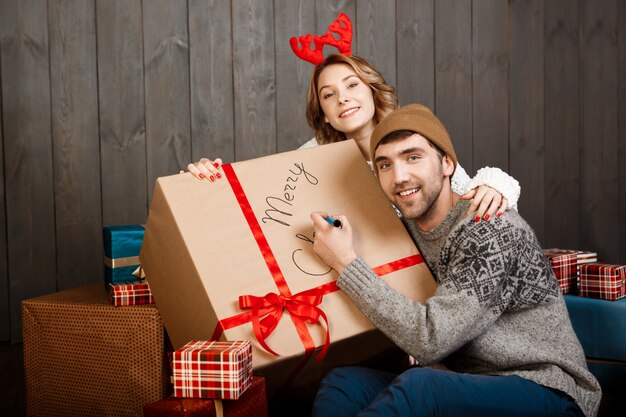 Man writing on gift box merry christmas sitting with girlfriend.