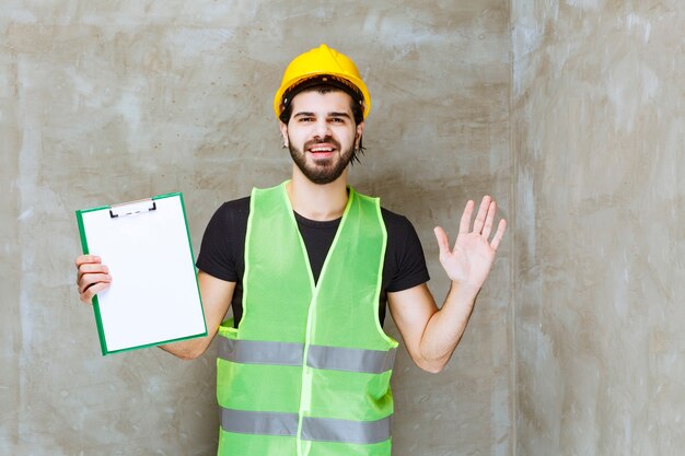 Man in yellow helmet and gear holding a project plan and looks confused