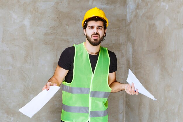 Man in yellow helmet and gear holding the project reports and looks unsure and thoughtful about them