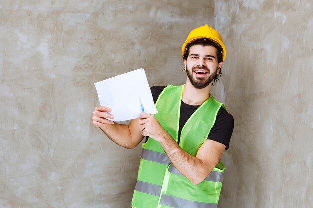 Man in yellow helmet and gear holding project reports