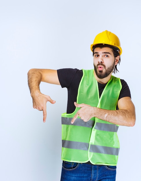 下に何かを示している黄色いヘルメットの男。