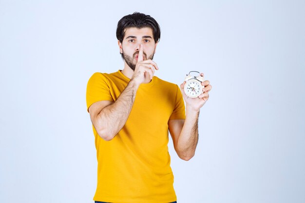 Man in yellow shirt holding an alarm clock and make silence gesture