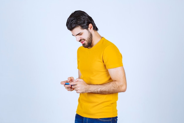 青いスマートフォンを持っている黄色いシャツの男。