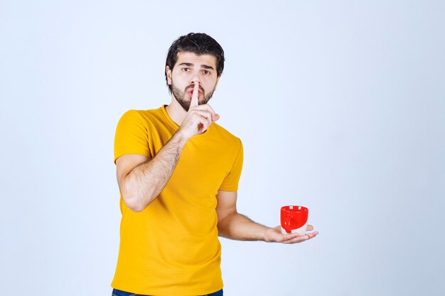 Man in yellow shirt holding a cup of coffee and looks mysterious.