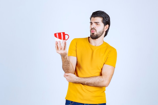 Man in yellow shirt holding a red cup and thinking.