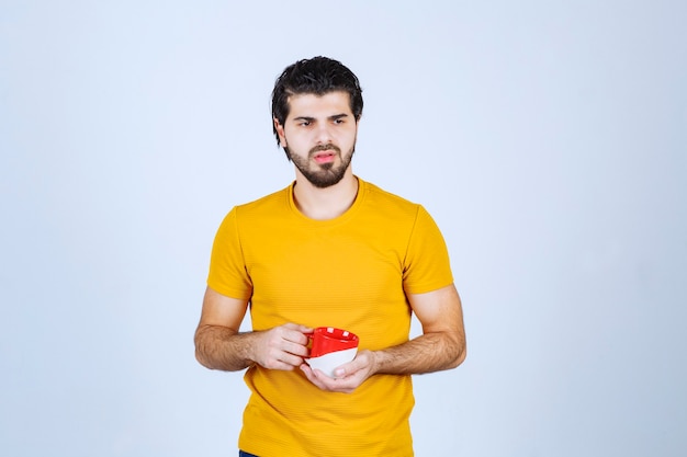 Man in yellow shirt holding a red cup and thinking.