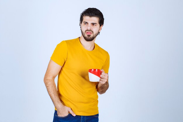 Uomo in camicia gialla che tiene una tazza rossa e pensa.