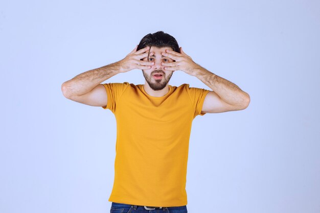 Man in yellow shirt looking through his fingers. 