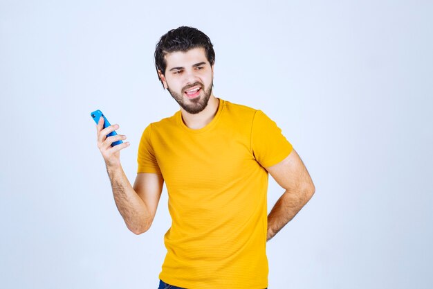 Man in yellow shirt pointing his smartphone and enjoying it.