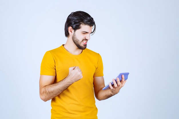 Man in yellow shirt working with calculator and looks happy because of results.