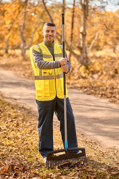 Foto gratuita un uomo con un giubbotto giallo con rastrello nel parco