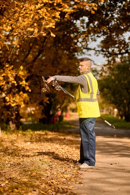 A man in a yellow vest with rake in the park