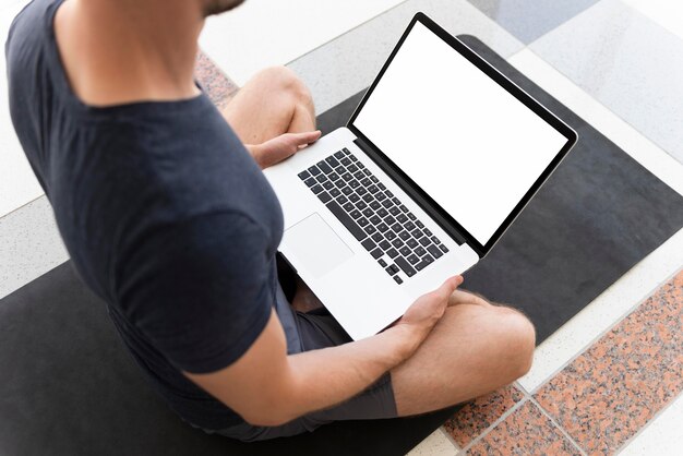 Man on yoga mat with blank laptop