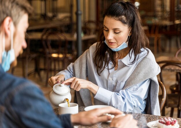 Mana and woman drinking tea with face masks on their chin