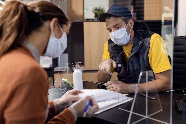 Manager of auto repair shop pointing at place of signature through sneeze guard