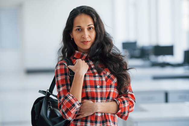 Manager has arrived to the office. Portrait of attractive young woman standing with black bag