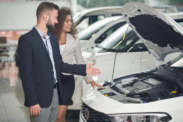 Manager showing car under hood to client in car center