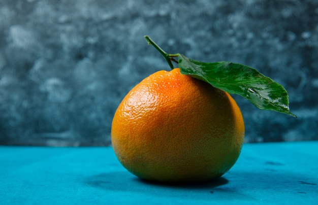 Mandarin orange with leaf side view on blue textured table and dark texture