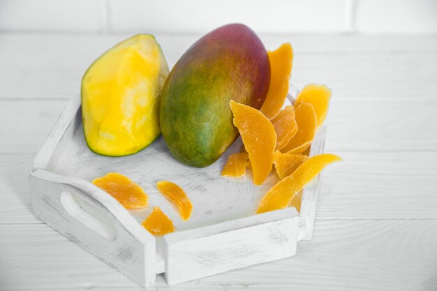 Манго на белом деревянном фоне с соком и сушеным манго на белом деревянном подносе, концепция здоровой пищи и экзотических фруктов
