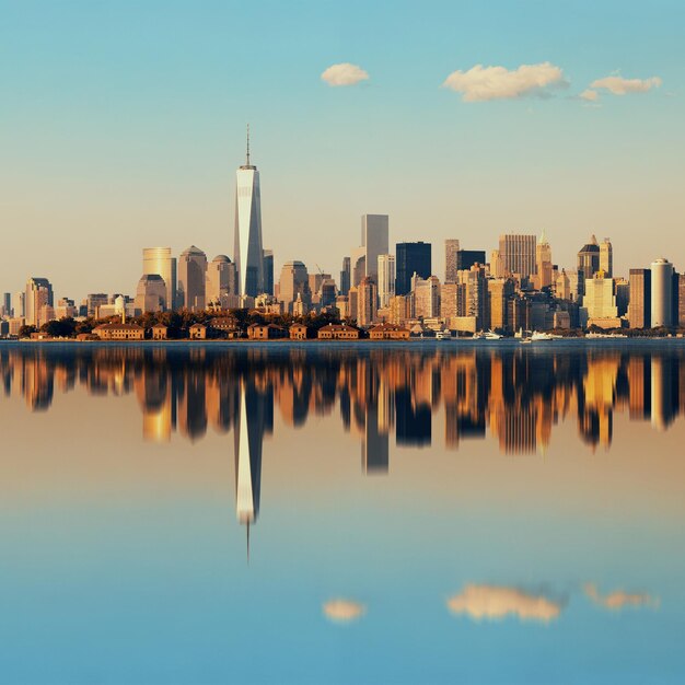 反射のある川の上の都市の高層ビルがあるマンハッタンのダウンタウンのスカイライン。
