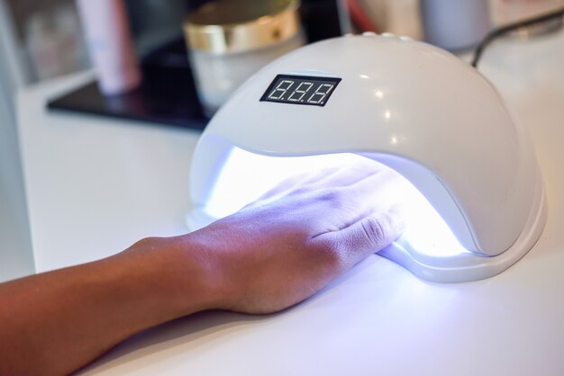 Manicured nails in UV lamp in beauty salon.