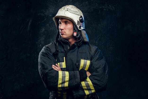 manly firefighter in helmet looks sideways in studio on black background