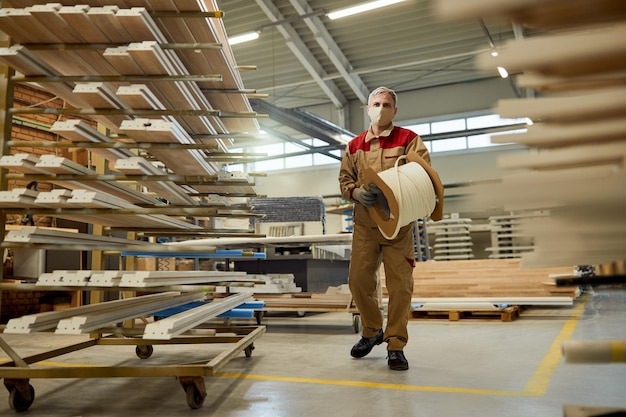 Manual worker with face mask carrying protective foam while working at carpentry warehouse