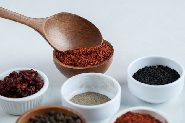 Many bowls of spices on a white surface.