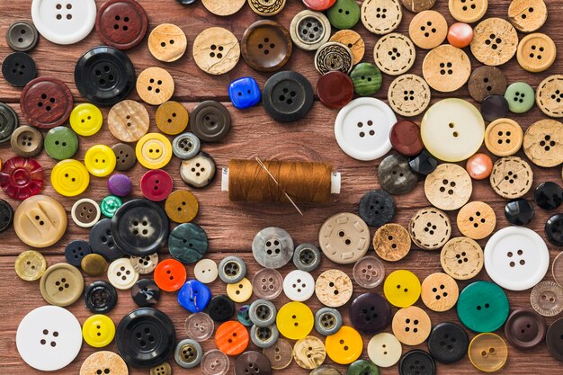 Many colorful buttons; brown thread and needle on wooden background