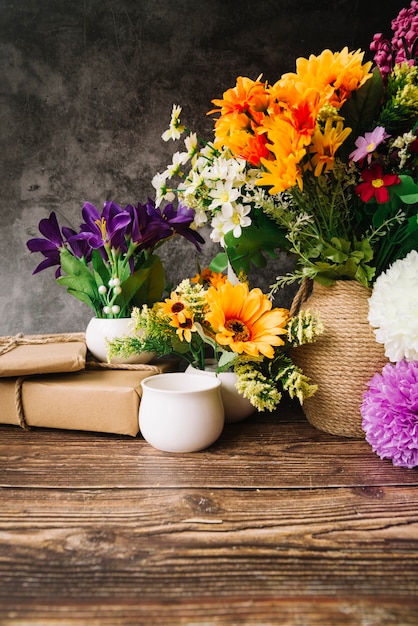 木製のテーブルにギフトボックスを持つ花瓶の多くのカラフルな花