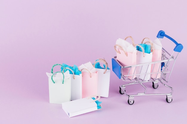 Many colorful paper shopping bags in cart on pink background