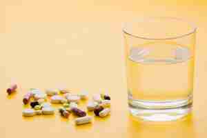 Free photo many colorful pills and glass of water on yellow background