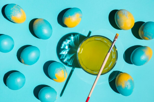 Many colourful Easter eggs with paint brush and glass of water 