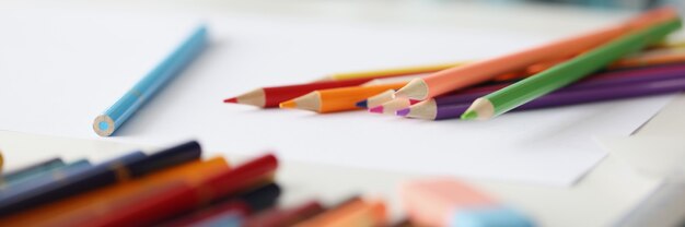 紙​の​クローズアップ​の​空白​の​シート​の​上に​横たわっている​多く​の​色とりどり​の​鉛筆
