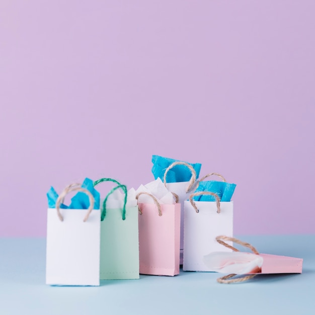 Many multicolored shopping paper bags in front of pink background