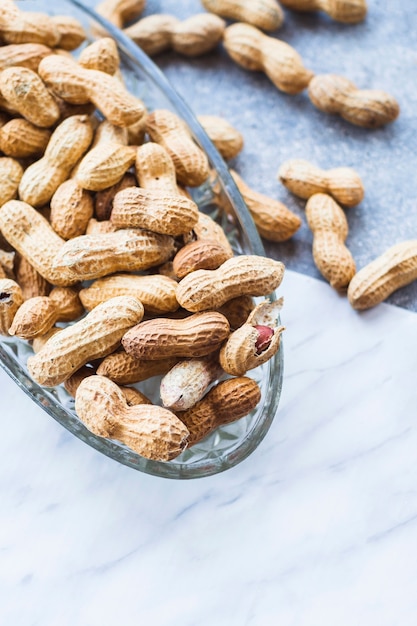 Many peanut shells in the glass bowl on marble backdrop