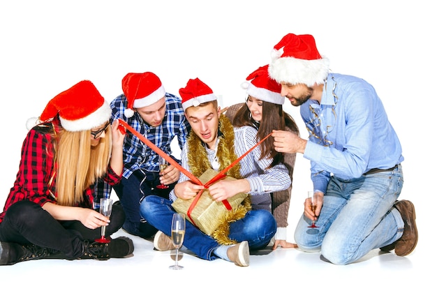 贈り物と白いスタジオの背景にクリスマスパーティーで飲む多くの若い女性と男性