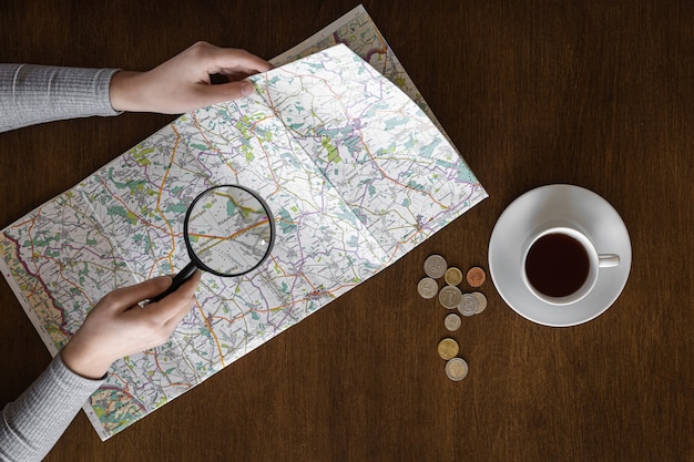 Map and magnifier in female hands on a wooden background top view