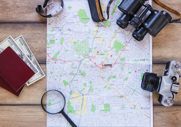 Map; passport; banknotes; magnifying glass; camera; binoculars and wrist watch on wooden backdrop