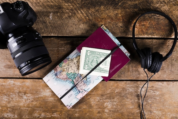 Map with passport, banknotes, headphone and DSLR camera on wooden surface