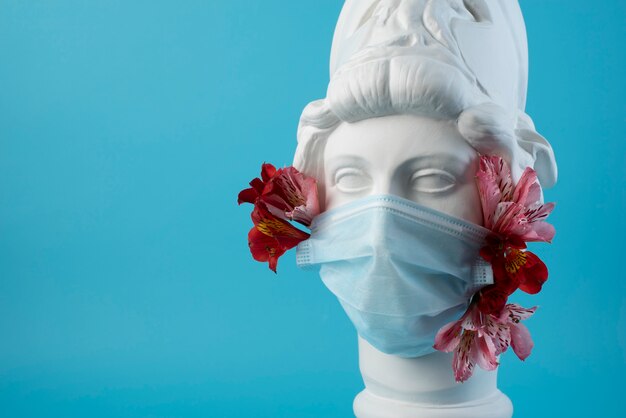 Marble sculpture of historical figure with medical mask and flowers