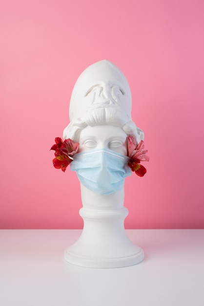 Marble sculpture of historical figure with medical mask and flowers