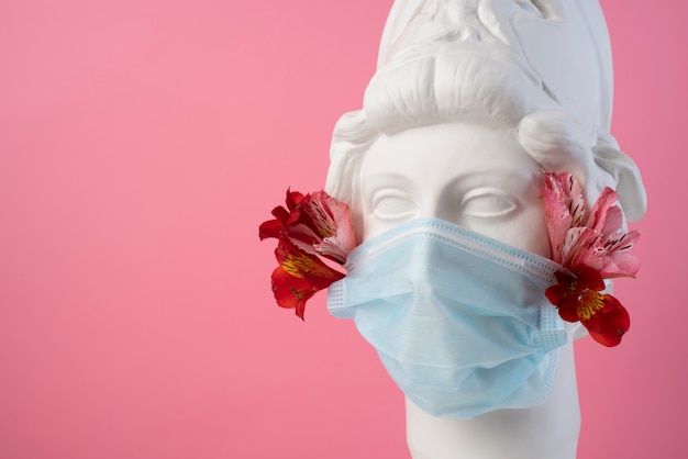 Free photo marble sculpture of historical figure with medical mask and flowers