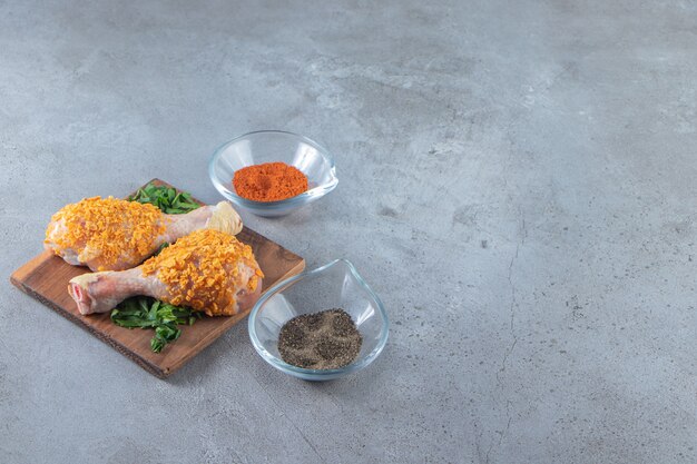 Marinated chicken drumstick on a greenery on a board , on the marble background.