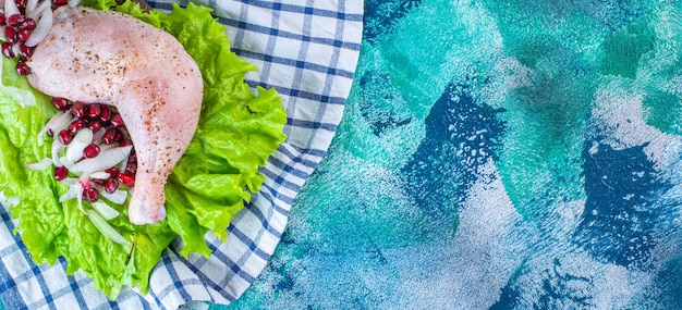 Marinated chicken drumstick with pomegranate arils on a lettuce leaves on a board on a tea towel on the blue background. High quality photo