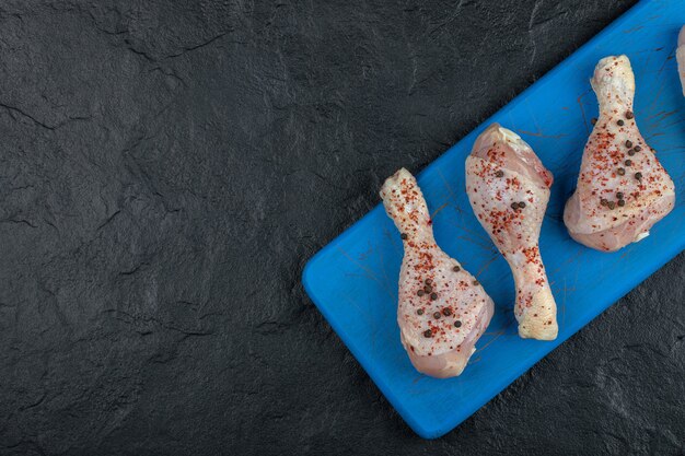 Marinated chicken drumsticks on blue wooden board.