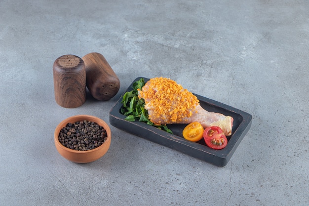 Marinated drumstick on a board next to spice bowl , on the marble surface.
